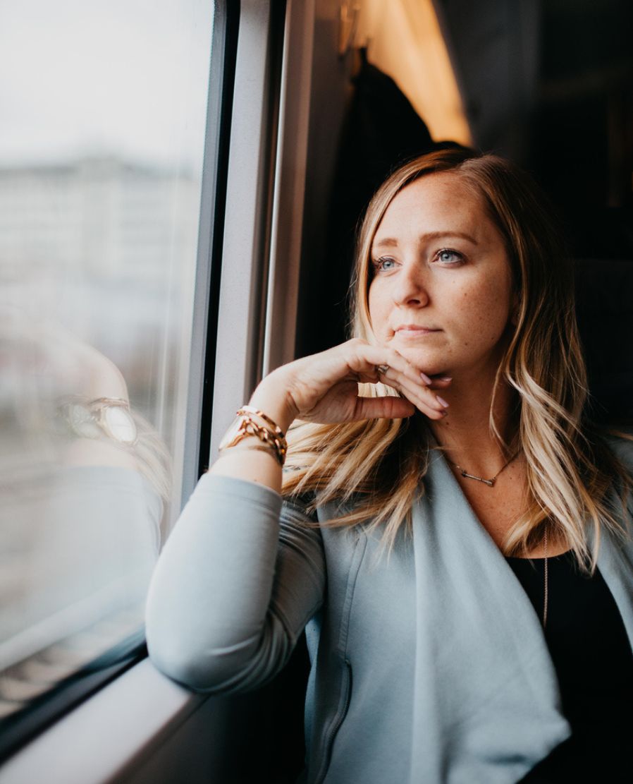 A woman sitting by a window, thoughtfully reflecting on her feelings and the stories she tells herself